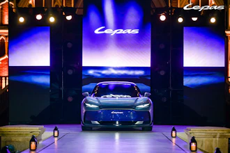 Luxury sports car displayed on stage during brand launch event with illuminated screens and dramatic blue lighting