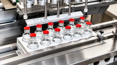 Pharmaceutical filling machine dispensing liquid into clear glass vials with red caps on production line