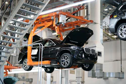 Black SUV suspended by orange mechanical lift in automotive manufacturing facility