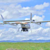 Agricultural drone flying over green field with mountains under blue sky