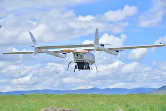 Agricultural drone flying over green field with mountains under blue sky