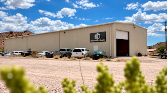 Surveying & Scale industrial warehouse building with metal siding and parked vehicles in desert landscape