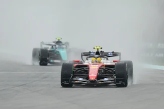 Formula 1 racing cars competing on a wet track in rainy conditions, with red and black vehicles leading the field.