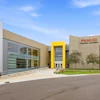Modern FANUC Training Academy building with glass and tan facade, featuring yellow accent entrance and landscaping
