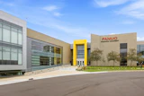 Modern FANUC Training Academy building with glass and tan facade, featuring yellow accent entrance and landscaping