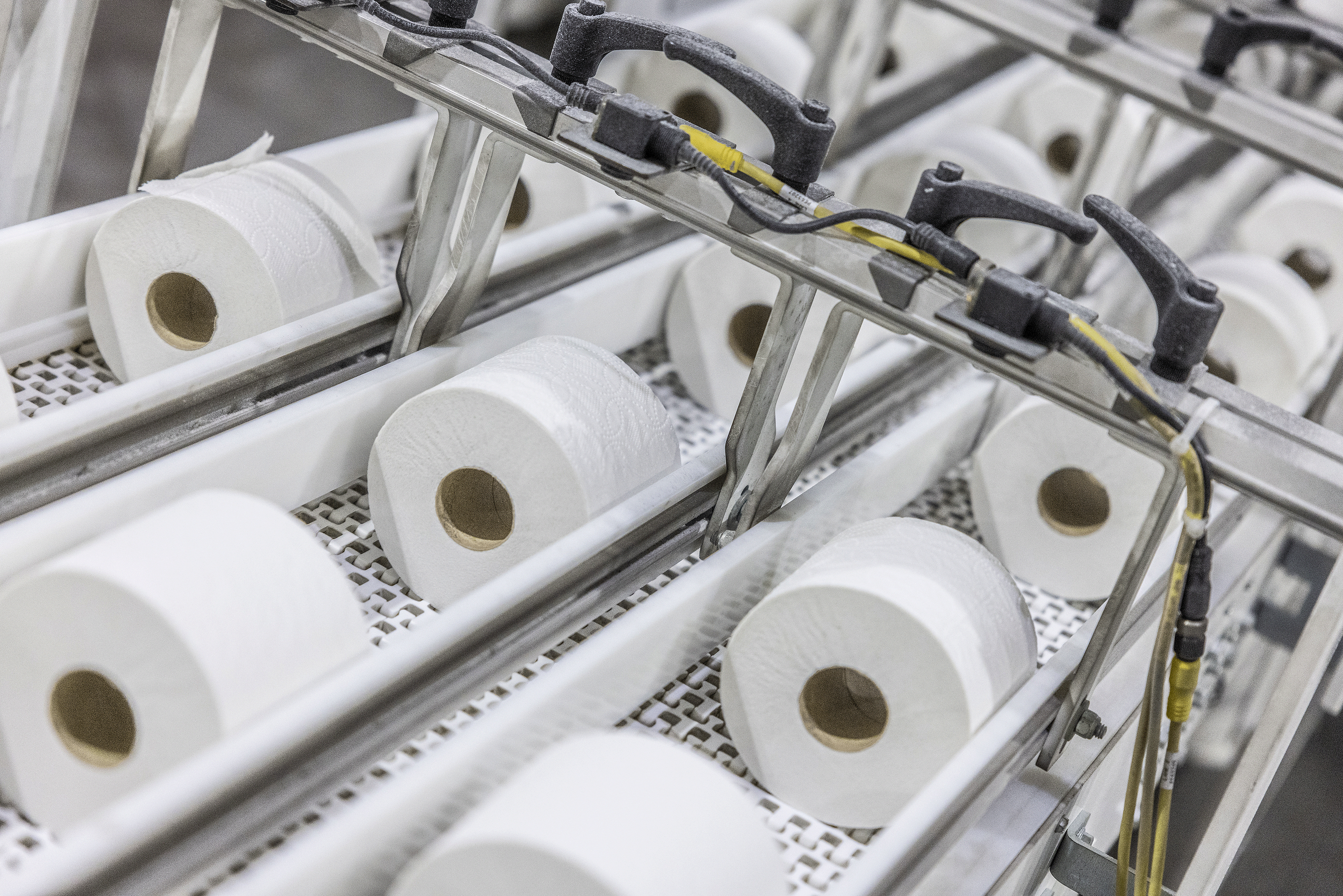 Industrial production line with multiple white tissue paper rolls on conveyor system with mechanical components and yellow wiring