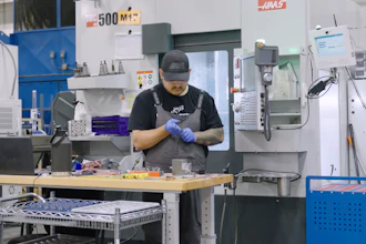 Machinist in blue gloves working at a HAAS CNC machine in an industrial manufacturing facility.