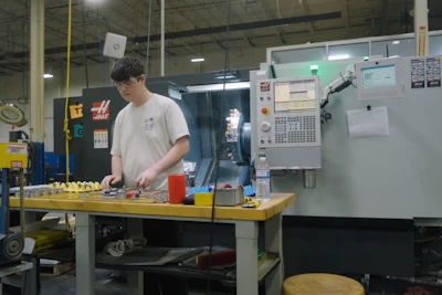 Machinist working at industrial workstation with CNC machine and tools in factory setting
