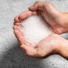 Hands holding white salt or sugar crystals against concrete background