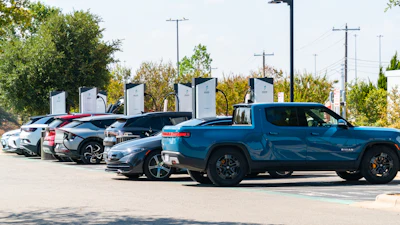 Row of electric vehicles charging at outdoor station with multiple chargers