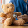 Healthcare professional using stethoscope to examine teddy bear during pediatric medical examination
