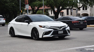 White Toyota Camry sedan parked on urban street with trees and buildings in background