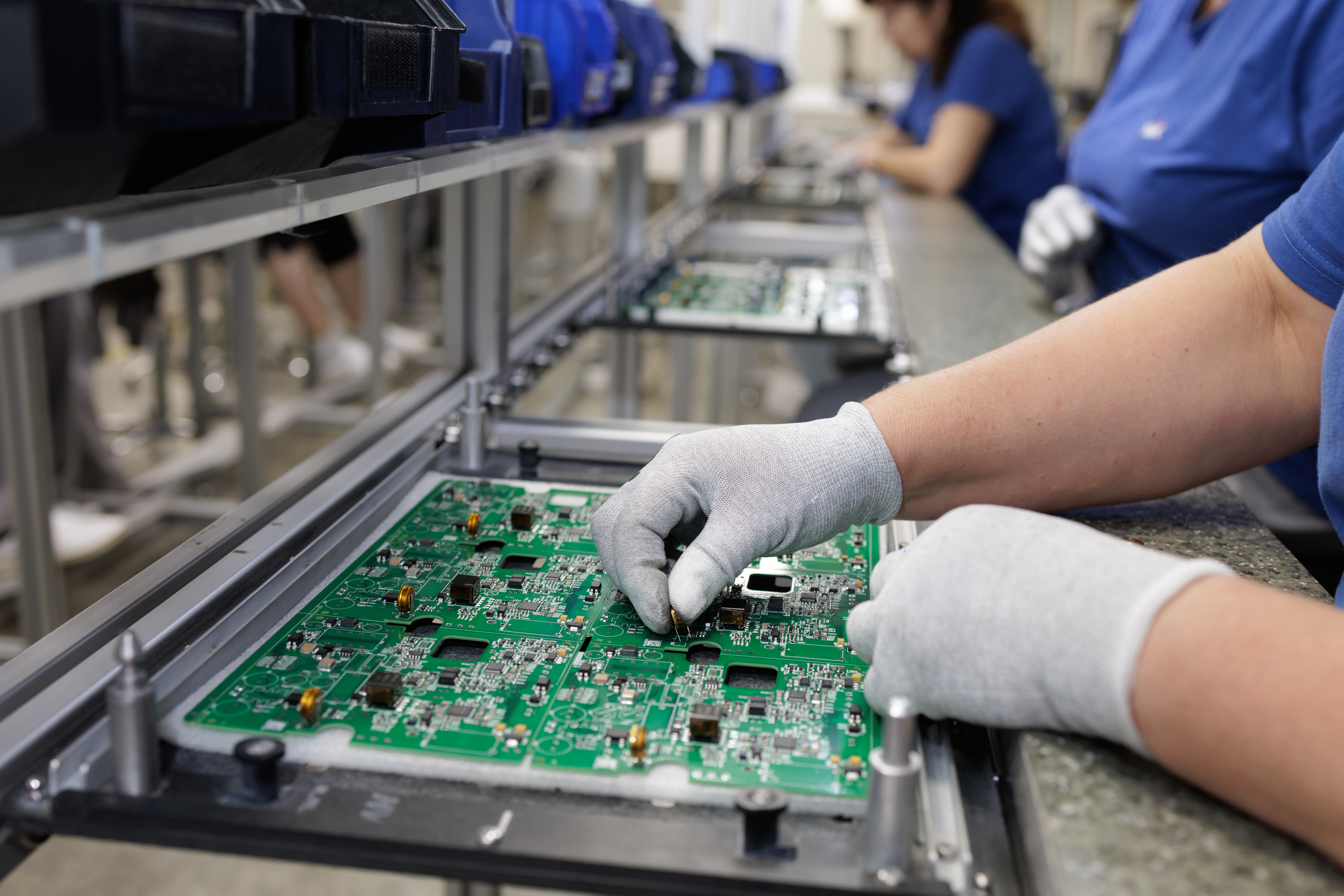 Electronics factory workers assembling and inspecting green circuit boards on an industrial production line