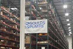 Industrial warehouse interior with tall storage racks, branded signage including Goulds Pumps and Rexnord logos, pallets, and orange safety markers on concrete floor.
