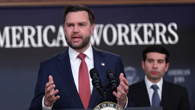 Man in navy suit speaking at podium with Presidential Seal, addressing audience at American Workers event