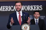 Man in navy suit speaking at podium with Presidential Seal, addressing audience at American Workers event