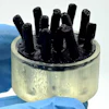 Black rod-like structures in clear cylindrical container against blue background