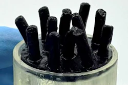 Black rod-like structures in clear cylindrical container against blue background