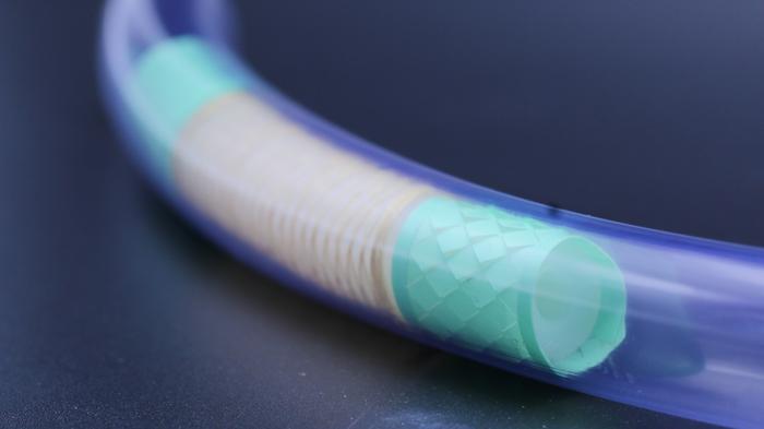 Blue flexible tube with cyan translucent sections showing internal mesh structure against dark background