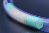 Blue flexible tube with cyan translucent sections showing internal mesh structure against dark background