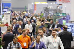 Crowded trade show floor with attendees wearing lanyards and ID badges networking among exhibition booths