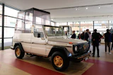 Vintage Mercedes-Benz G-Class with white body and gold wheels displayed in modern showroom with visitors
