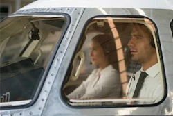 Two people seated in vintage aircraft cabin with sunlight streaming through windows