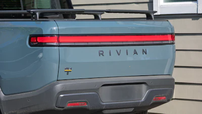 Rear view of light blue Rivian R1T electric truck with red horizontal tail lights and gray bumper