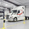 White Schneider semi-truck with red stripe parked in industrial warehouse facility with yellow safety barriers