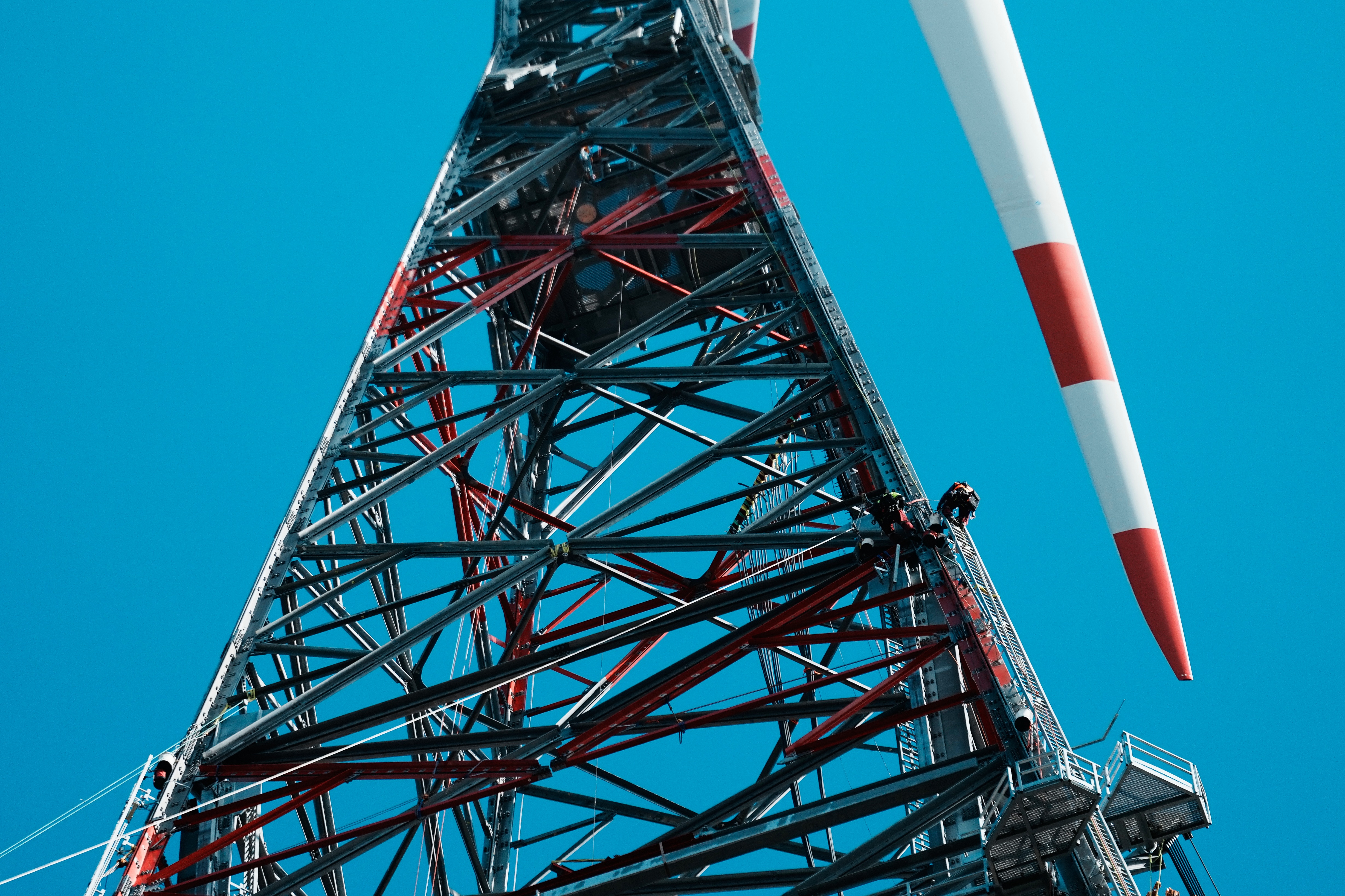 Tall telecommunications tower with red and white striped antenna against clear blue sky