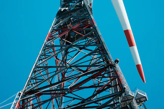 Tall telecommunications tower with red and white striped antenna against clear blue sky