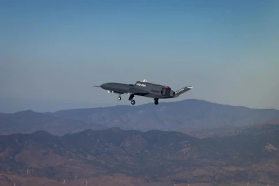 Dark aircraft in flight over mountainous terrain with clear blue sky